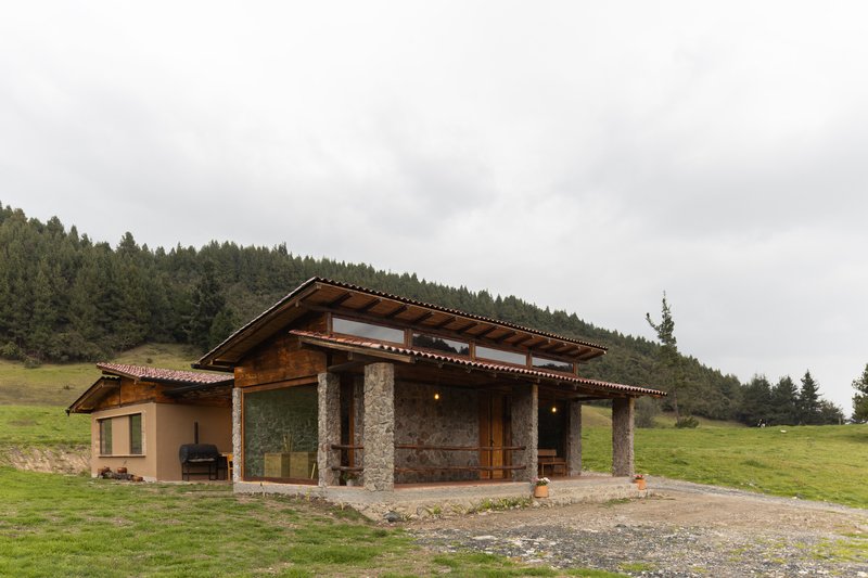 Pavilion with stone columns and deep overhanging eaves set against forested hillside under cloudy skies