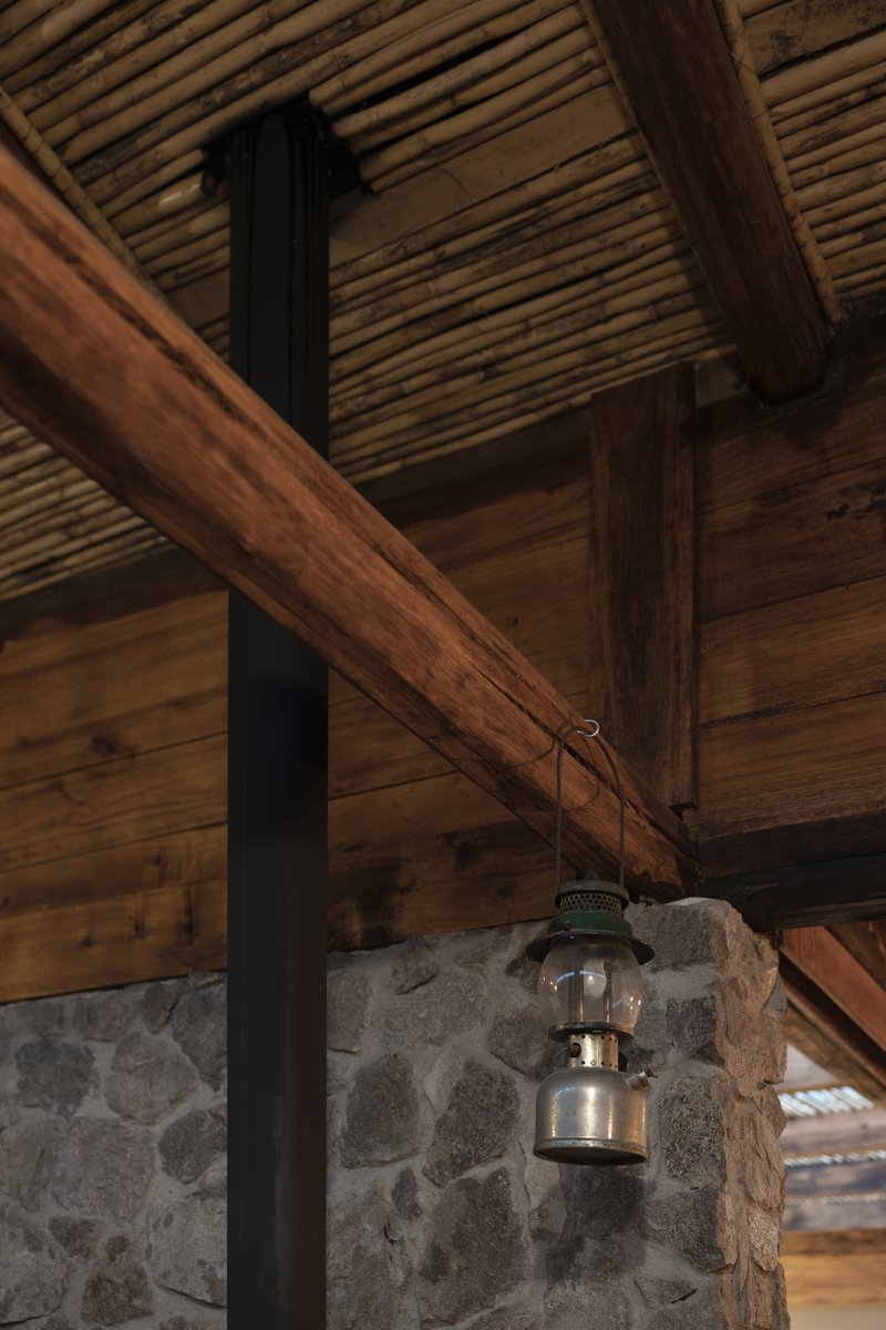 Detail of lantern hanging from timber beam junction beside stone wall and black steel flue pipe