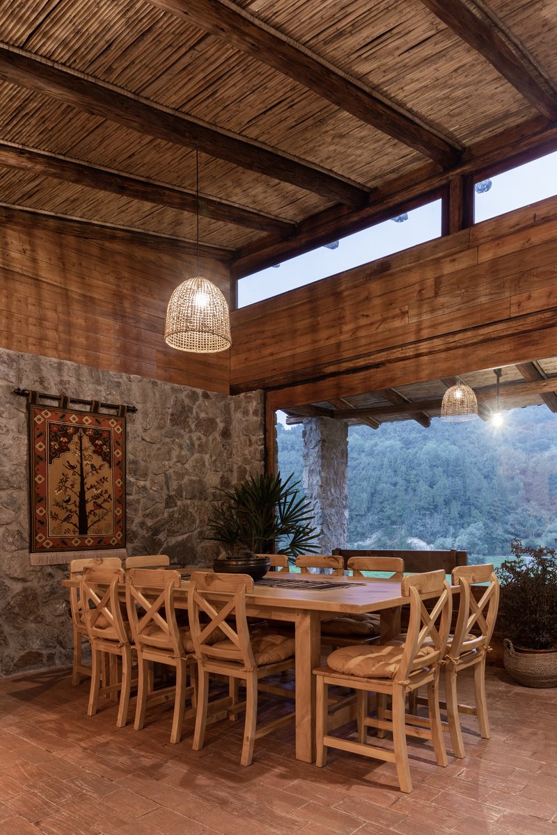 Covered dining terrace with exposed timber beams, stone walls and woven pendant lights at dusk