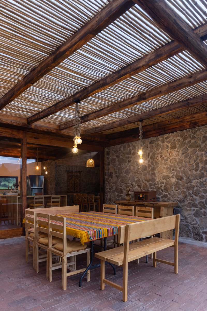 Outdoor dining area with slatted timber ceiling, stone masonry walls and pendant bulbs at dusk