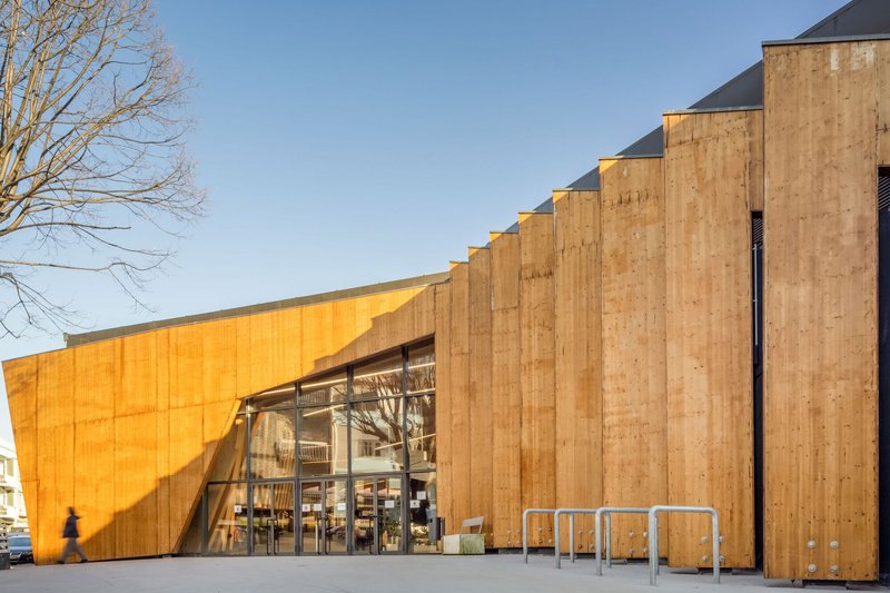 Oblique view of the timber-clad facade with vertical buttresses and glazed entry in afternoon light