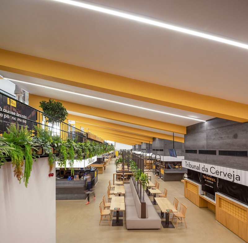 Food hall seating area with yellow ceiling beams, hanging planters and polished concrete floor