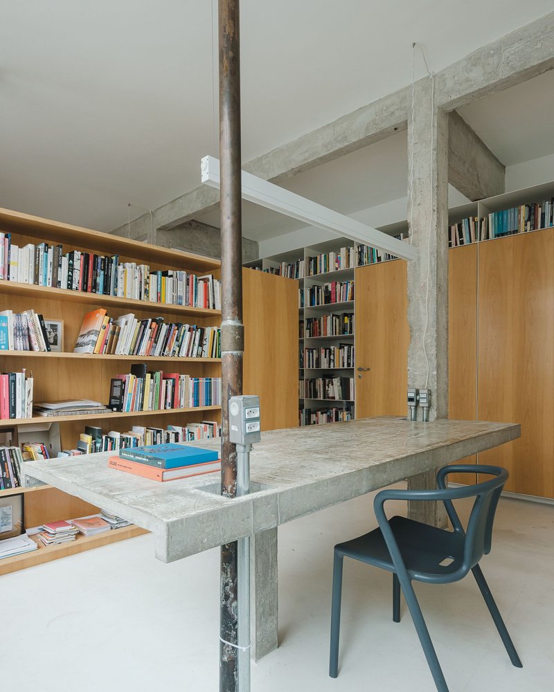 Library corner with blonde wood and built-in shelving flanking the concrete table and steel pipe