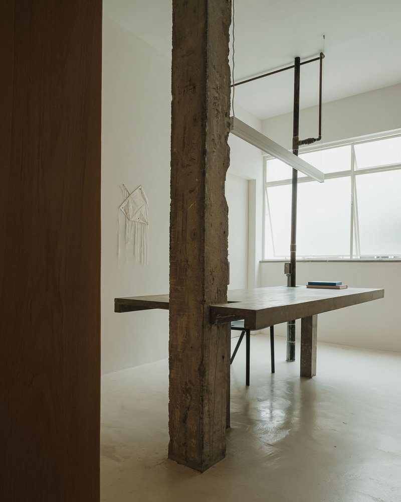 Concrete table integrated with a rough structural column beneath suspended lighting fixtures