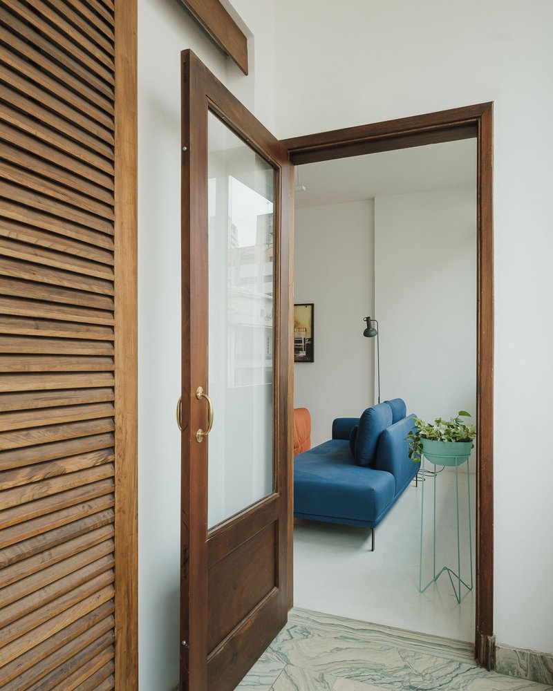 Dark timber-framed glass door opening from slatted screen hallway to living room with blue sofa