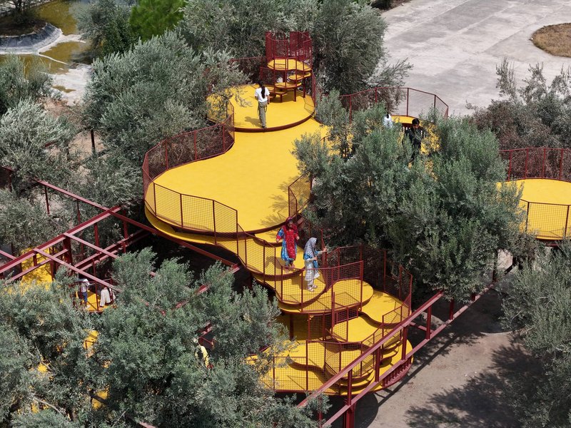 Elevated walkway with yellow metal mesh decking winding through olive trees with children playing below