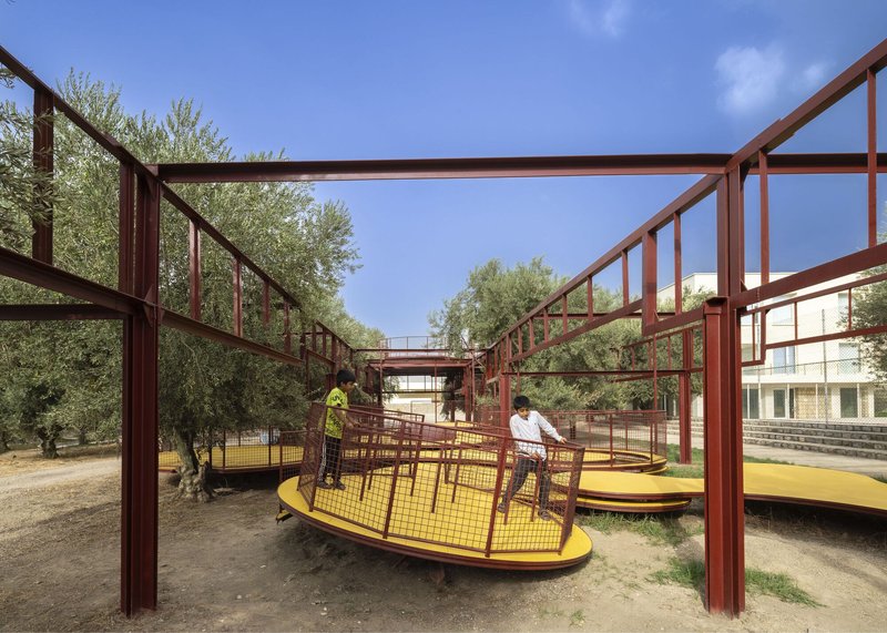 Red steel frame structure with yellow platforms weaving between olive trees under a clear blue sky