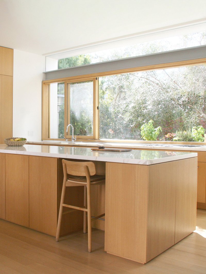Kitchen island with white stone countertop facing timber-framed windows overlooking a garden