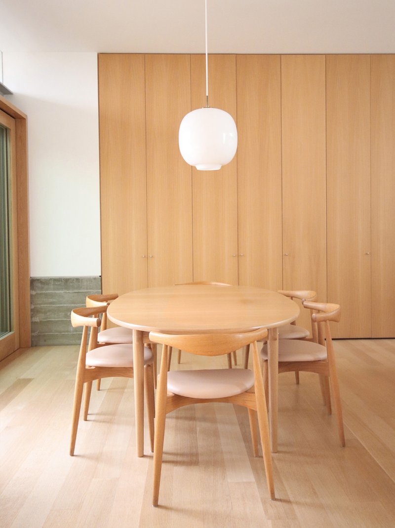 Dining room with round timber table and pendant light against floor-to-ceiling wood paneling