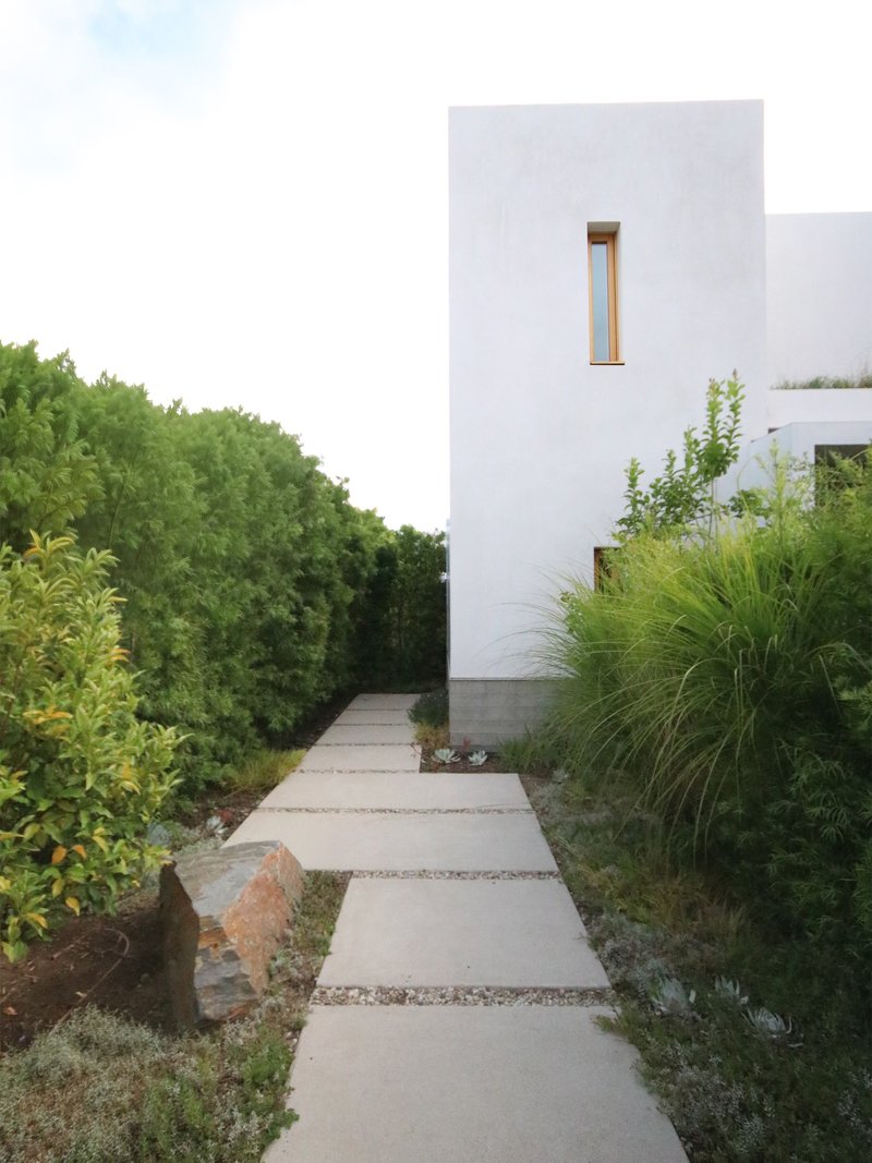 Concrete paver path flanked by grasses and plantings leading to a white stucco tower volume