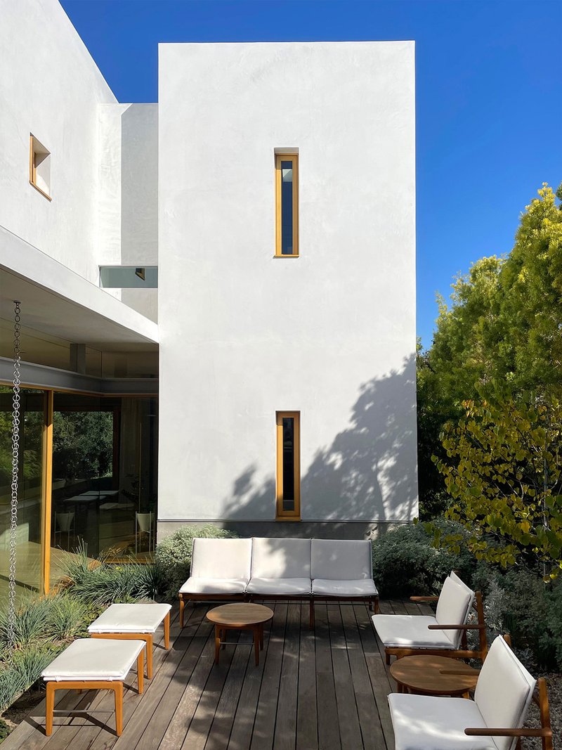 Outdoor terrace with timber lounge furniture beneath a white stucco facade with vertical slot windows