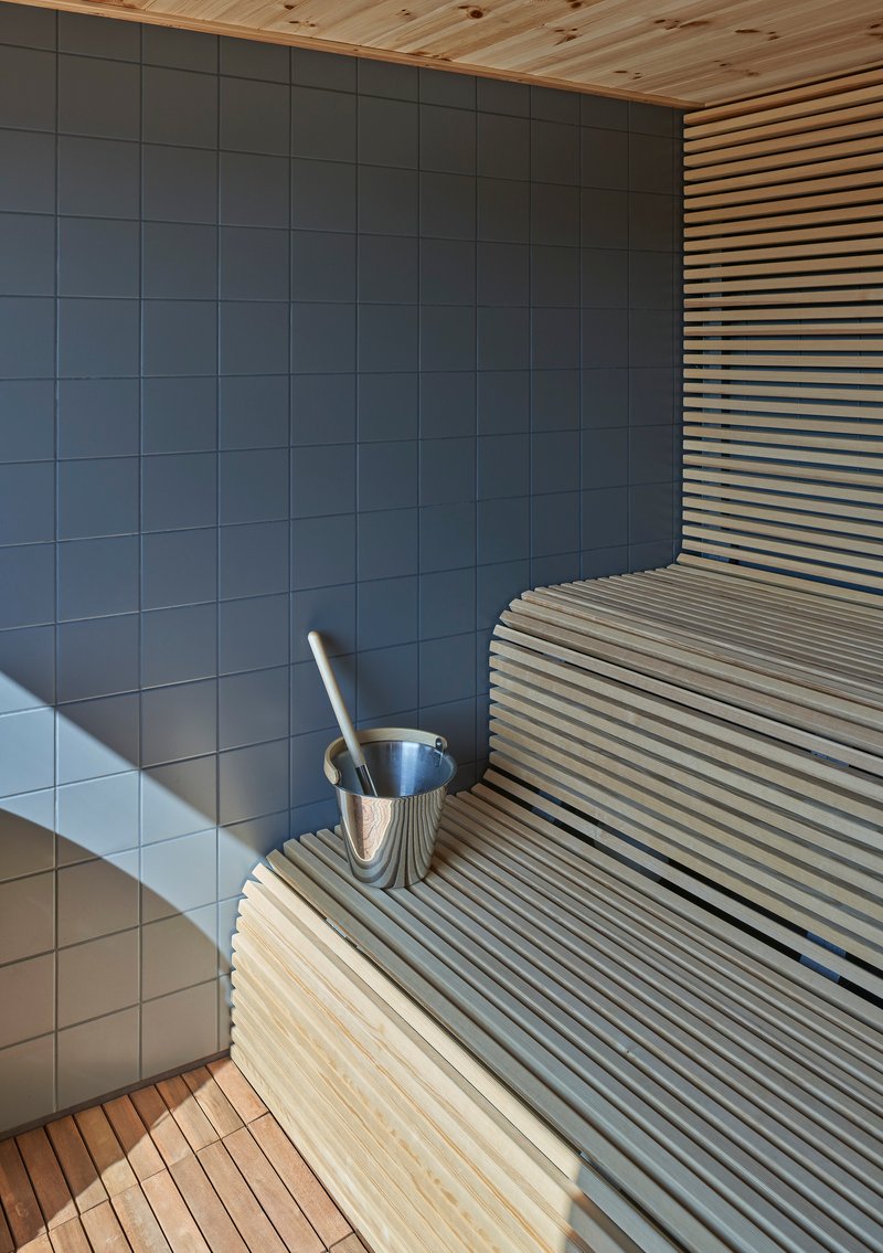 Sauna interior with horizontal slatted benches and grey tile wall beneath timber ceiling