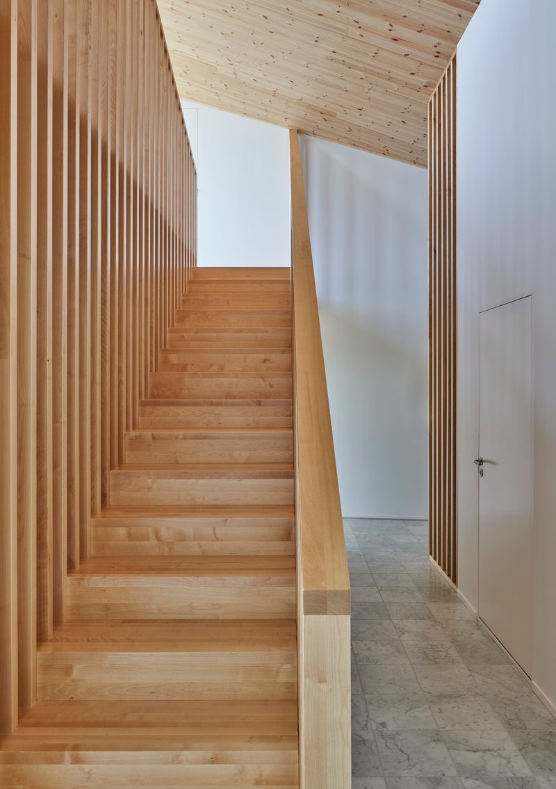 Timber staircase with vertical slat balustrade ascending beneath an angled plywood ceiling