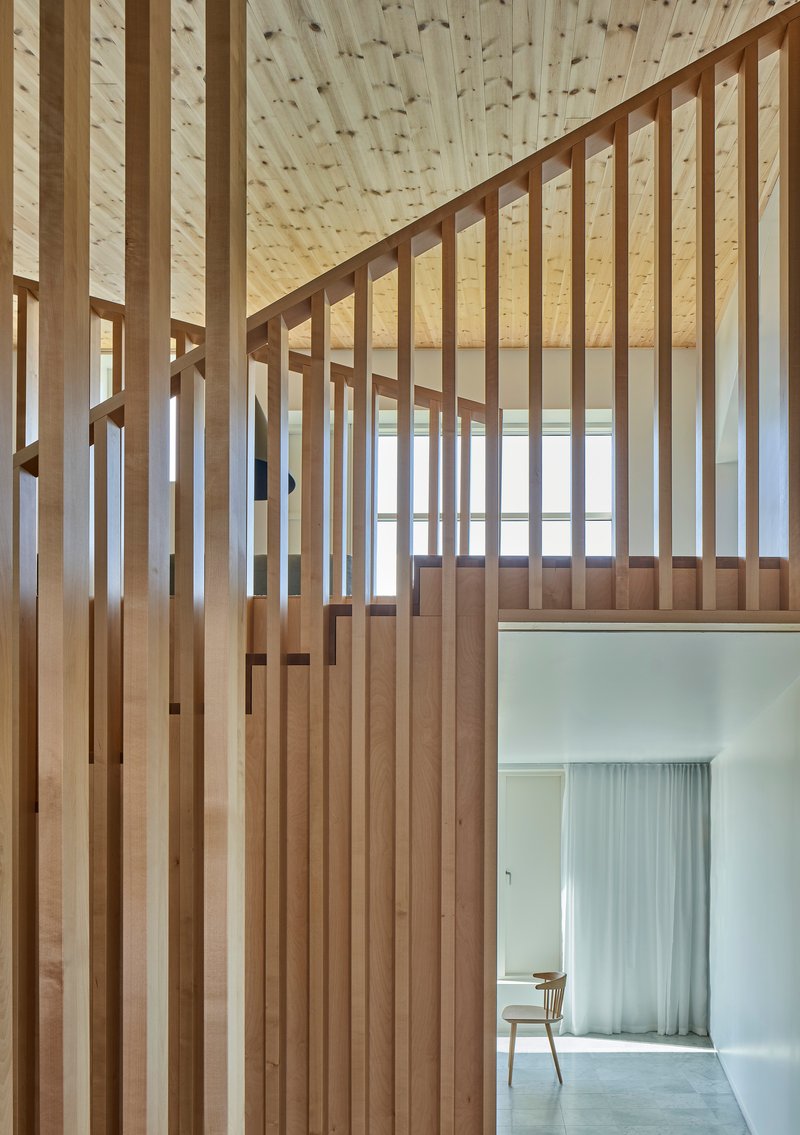 Double-height space with timber slat partitions framing an upper landing and doorway to a curtained room beyond