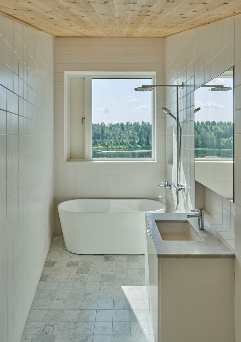 Bathroom with freestanding tub and picture window framing views of forest and lake