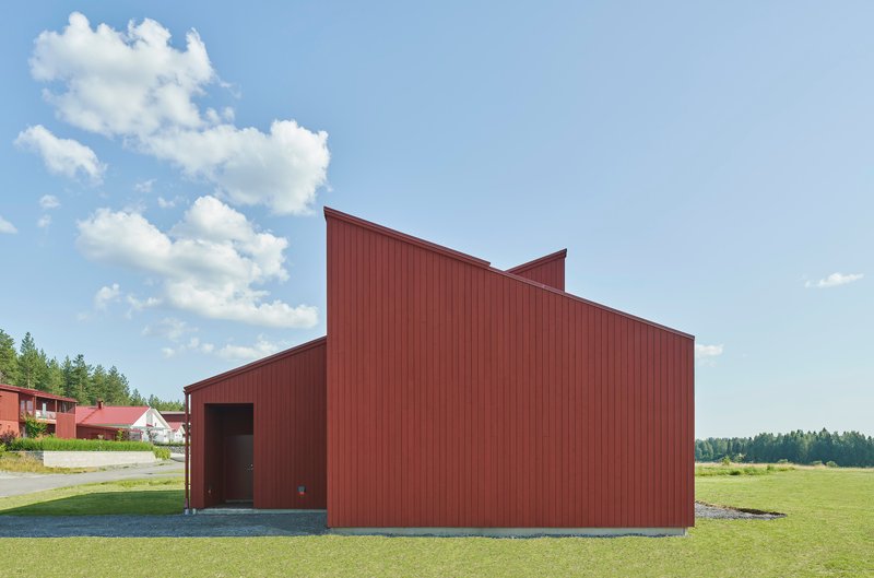 End view of the red corrugated metal facade with stepped roofline against a summer sky