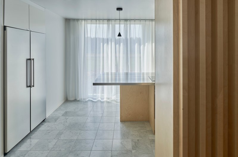 Kitchen with pale wood island and sheer curtains filtering light across grey tile floor
