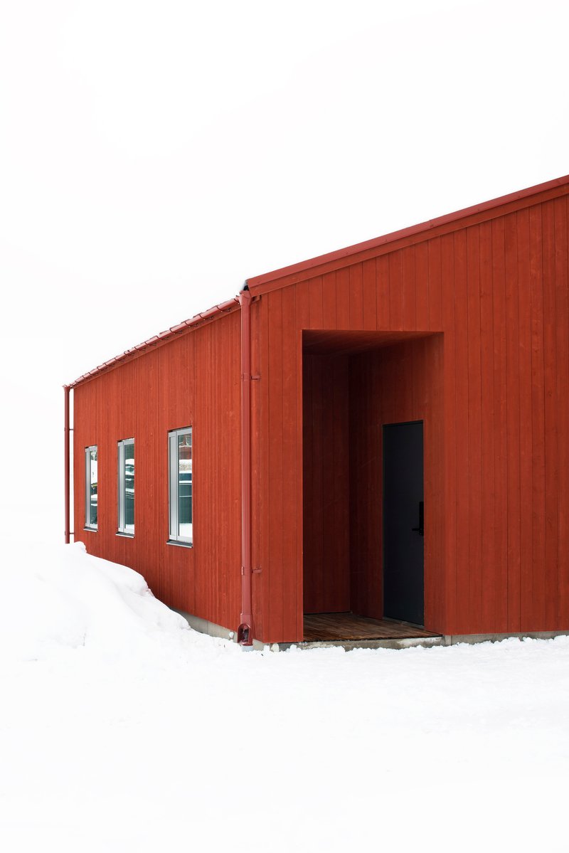 Recessed entrance in red wood cladding with a row of narrow windows in heavy winter snow