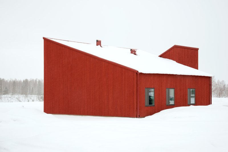 Angular red clad volumes with snow-covered roofs and three small windows set in a winter landscape