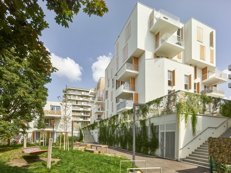 Courtyard view showing staggered white balconies and a green wall with climbing plants under blue sky