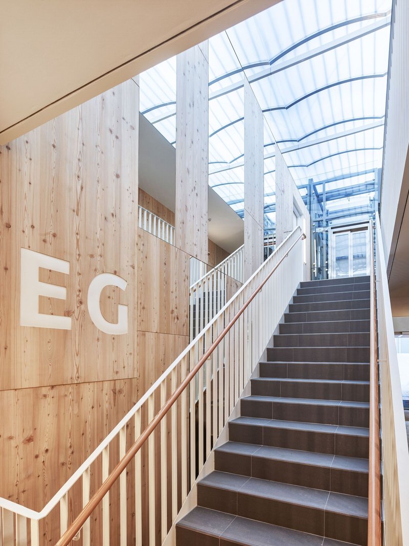 Interior stairwell with timber cladding and translucent polycarbonate skylight above grey tile steps