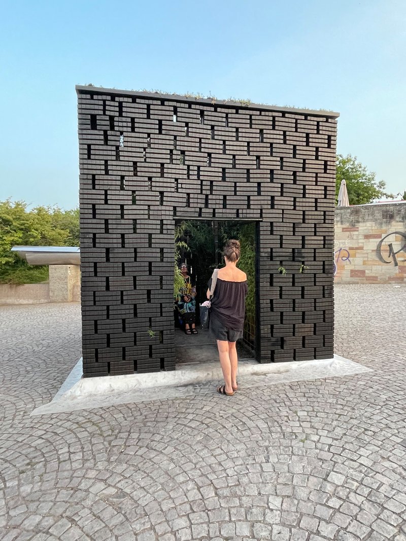 Woman entering basketweave brick pavilion with arched doorway on a cobblestone plaza in evening light