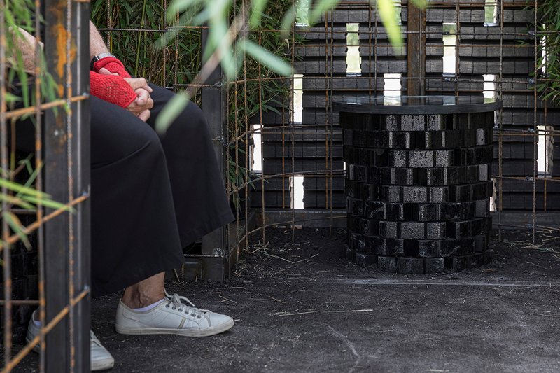Interior view through woven brick walls with openings filtering light and vegetation visible outside