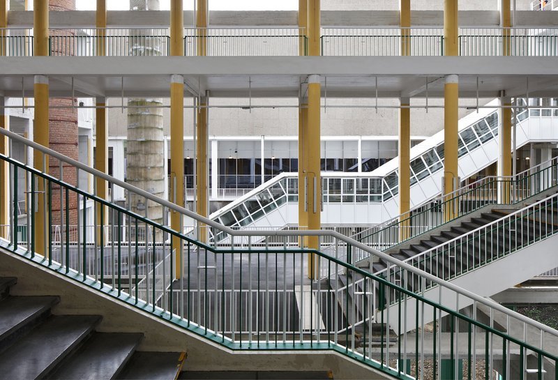Interior atrium showing curved staircases and yellow columns beneath a diagonal skylight structure