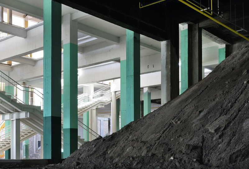 Interior view with turquoise columns and a dark earthen slope rising through the floor