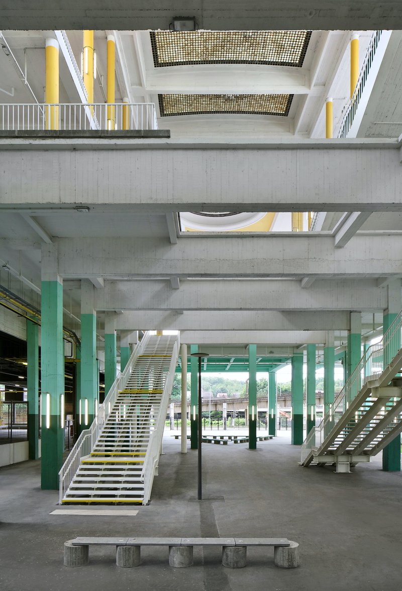 Ground floor interior with green columns, open steel stairs, and concrete bench beneath exposed structural beams