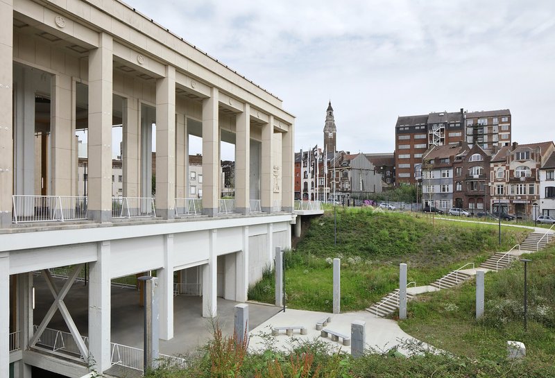 Elevated colonnade with precast columns overlooking a grassed embankment and surrounding urban buildings