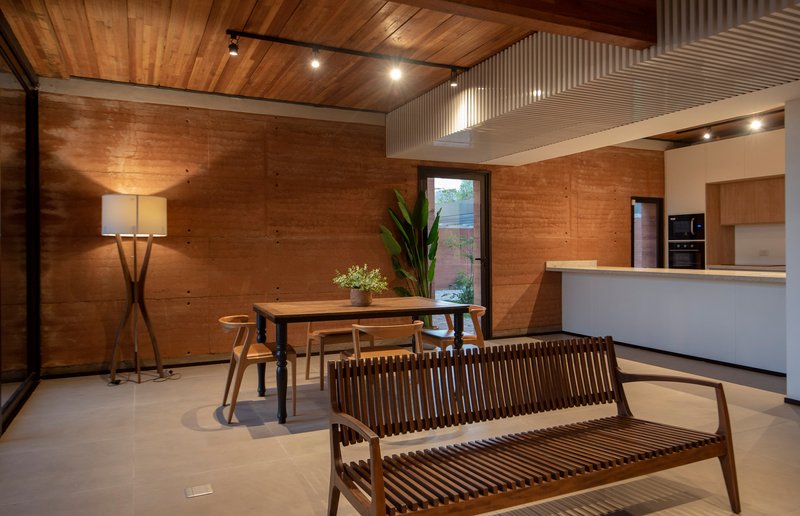 Open-plan living and dining space with rammed earth walls, timber ceiling and corrugated metal air duct