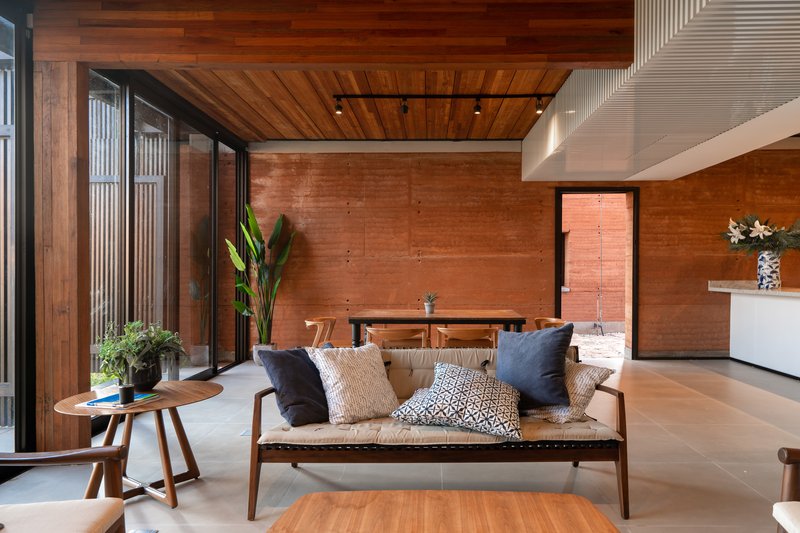 Living space with timber ceiling, rammed earth walls and glazed courtyard overlooking a potted plant