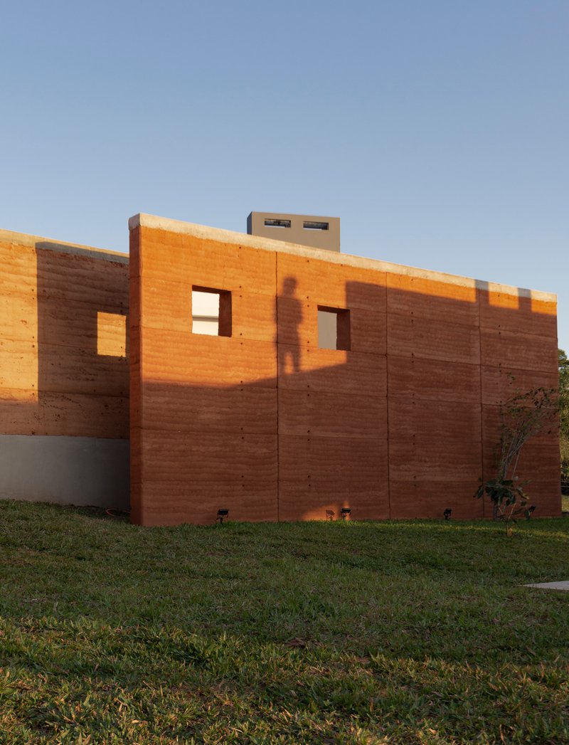 Exterior wall of horizontal rammed earth layers with punched window openings at dusk