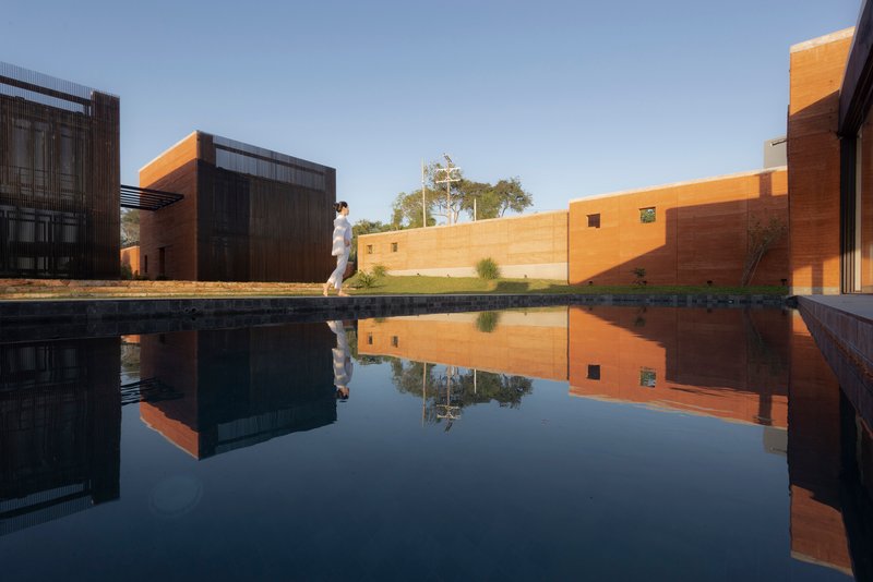 Reflecting pool mirroring the corrugated metal and rammed earth facades with a figure walking