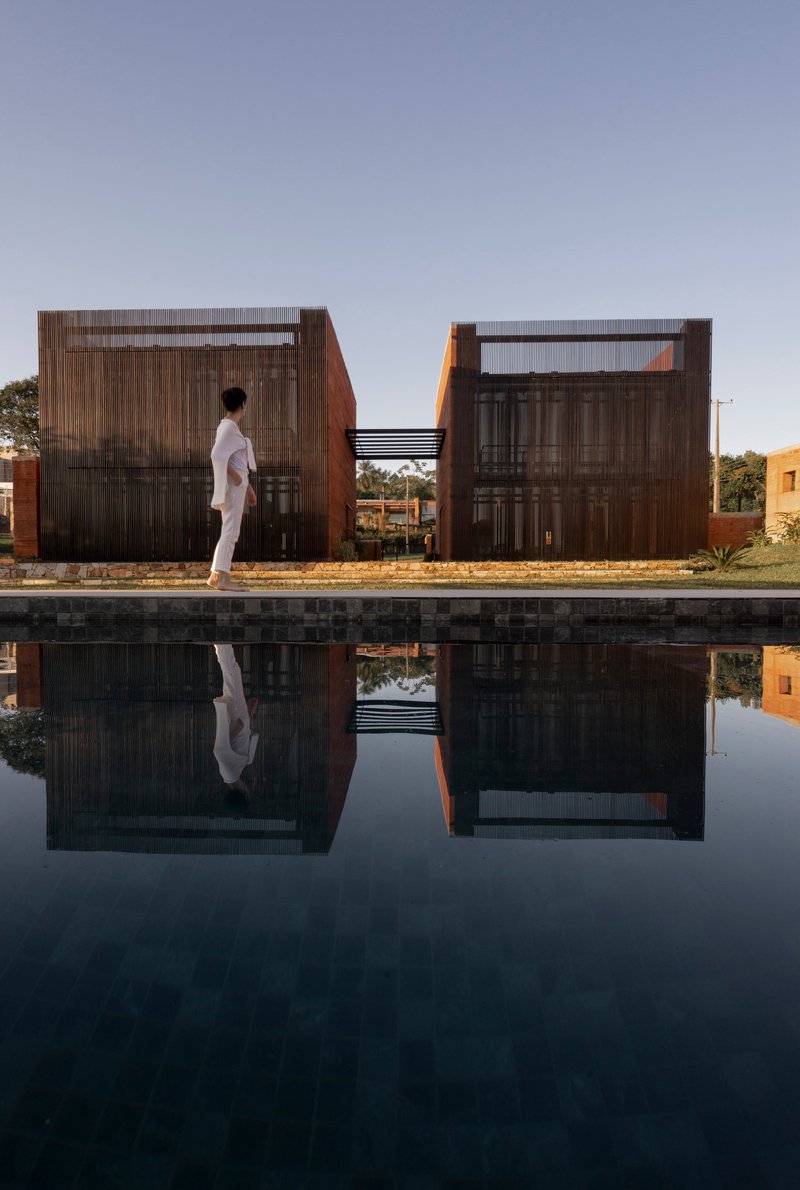 Figure walking beside reflecting pool with corrugated metal screen facades at dusk