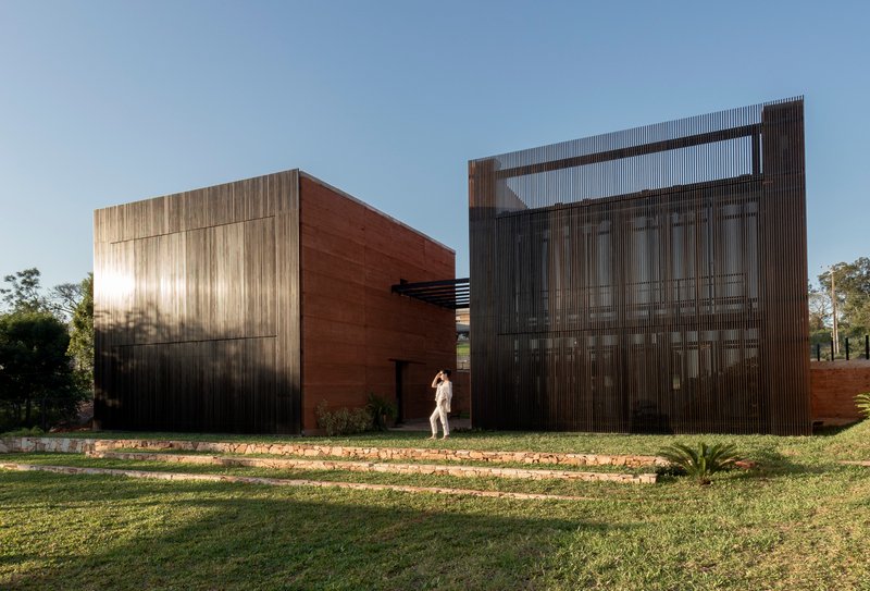 Frontal view of corrugated metal screen and rammed earth volumes in low afternoon sun