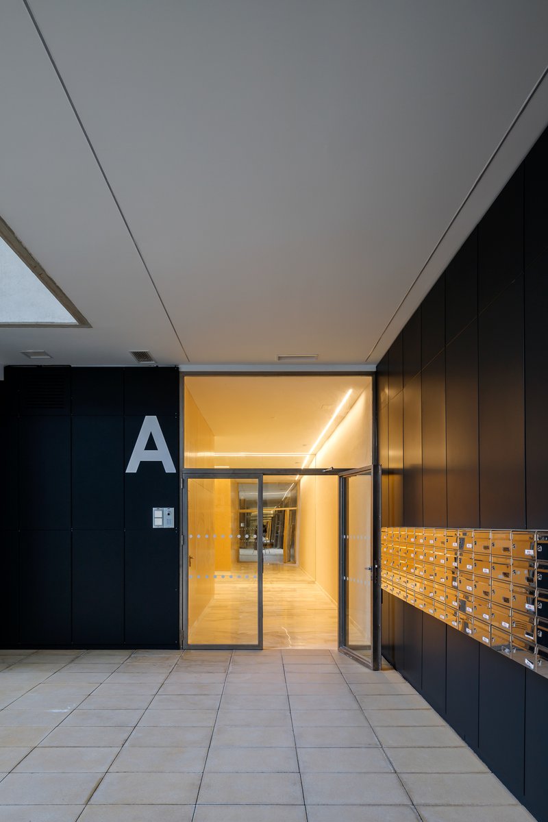 Ground floor lobby corridor with black paneling, illuminated yellow mailbox wall and glass entrance door