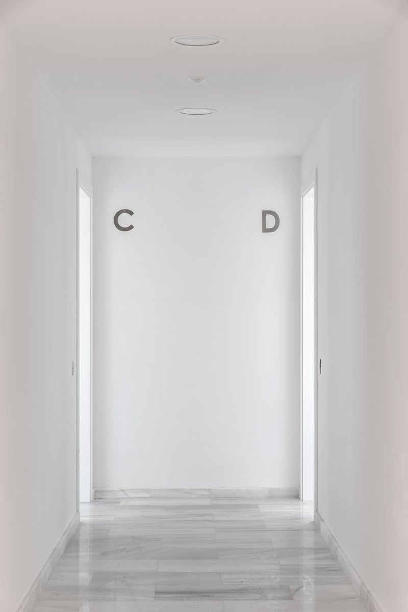 White corridor with pale timber flooring leading to a backlit wall marked with letters C and D