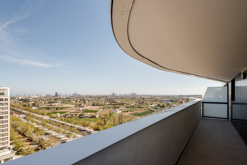 Balcony with curved soffit and white parapet overlooking patchwork farmland under clear blue sky