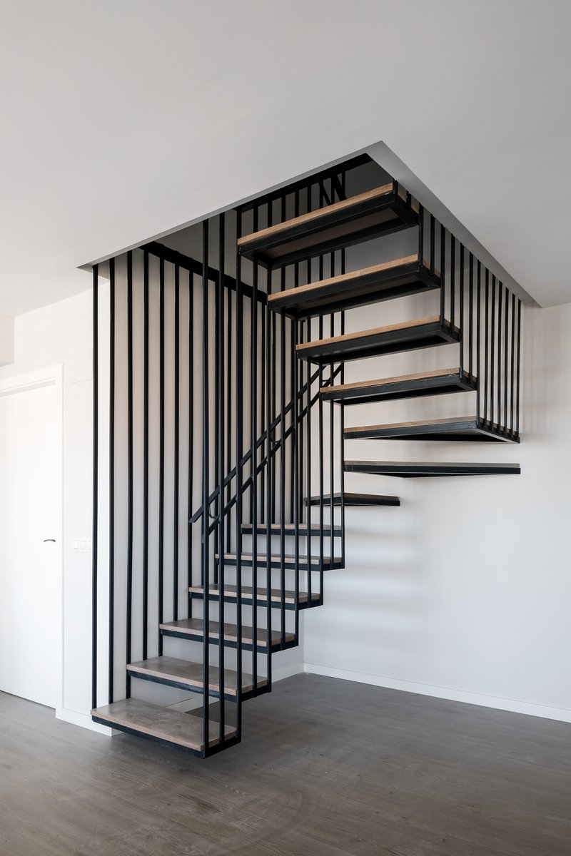 Black steel and timber staircase with vertical rod balustrade ascending through a white interior
