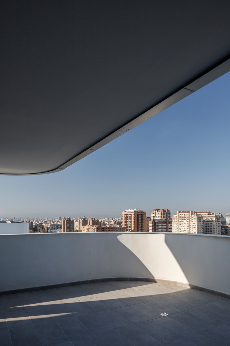 Rooftop terrace with curved dark soffit and white parapet framing distant residential towers at dusk