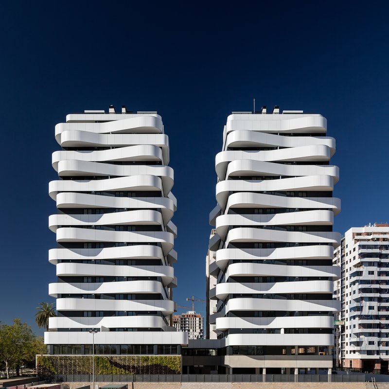 Twin residential towers with stacked ribbon balconies under a deep blue sky