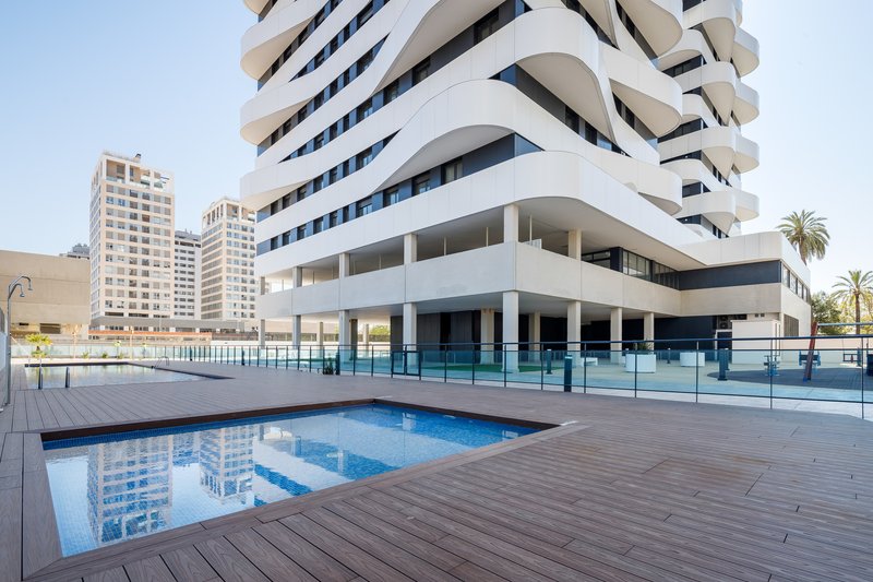 Ground-level pool deck with timber decking and glass railing below the curved balconies