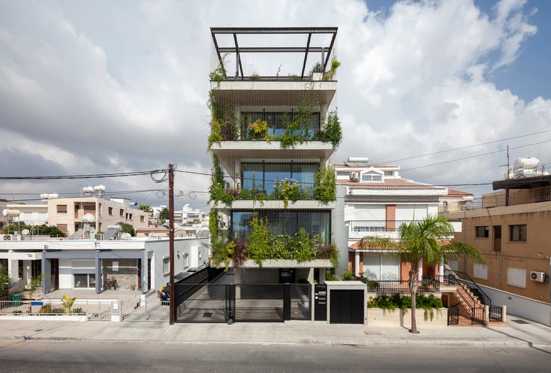 Front elevation showing stacked planted terraces between vertical louvers and neighboring residential buildings