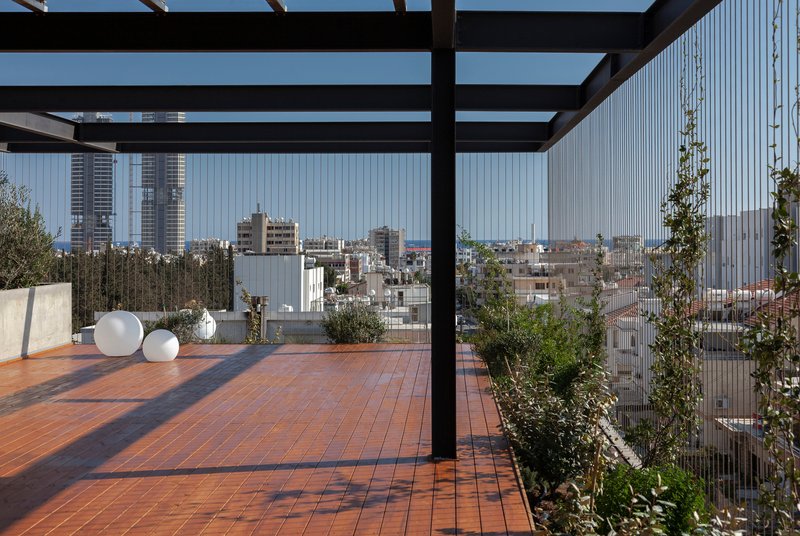 Steel pergola framing city views above terracotta tile terrace with potted plants and vertical screens