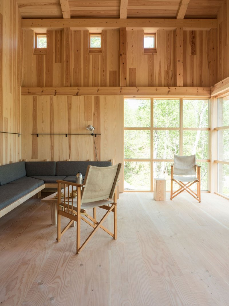 Living area with exposed timber beams, clerestory windows, and paired canvas chairs facing glazed wall