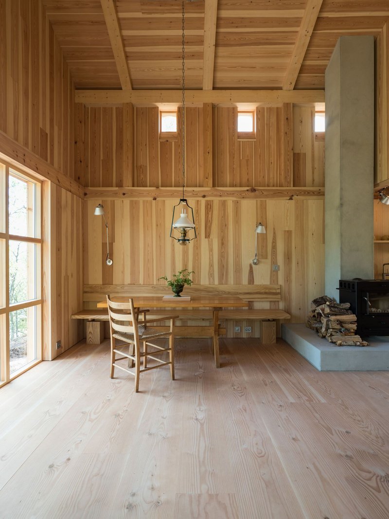 Dining area with pendant lights suspended above a table and concrete fireplace hearth with stacked firewood