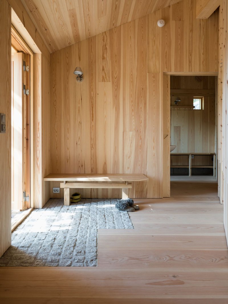Timber-lined entryway with built-in bench, textured rug, and view through to interior room beyond