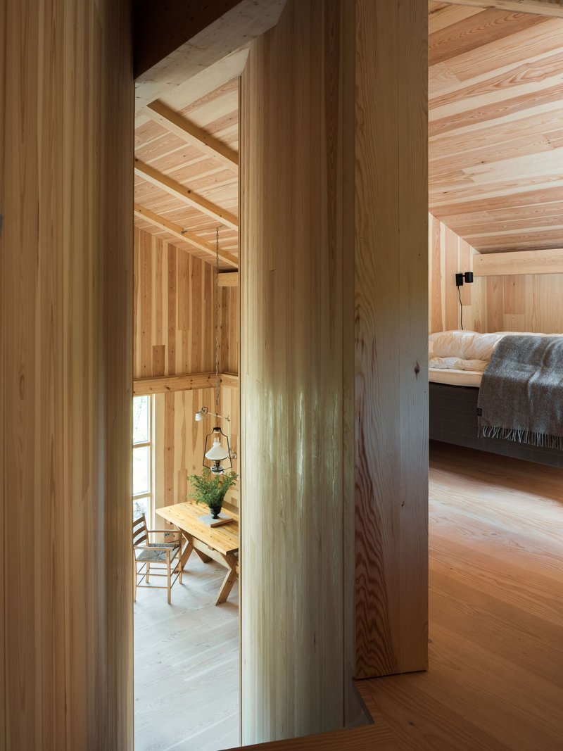 View through vertical wood columns toward dining area with hanging pendant and bedroom in background